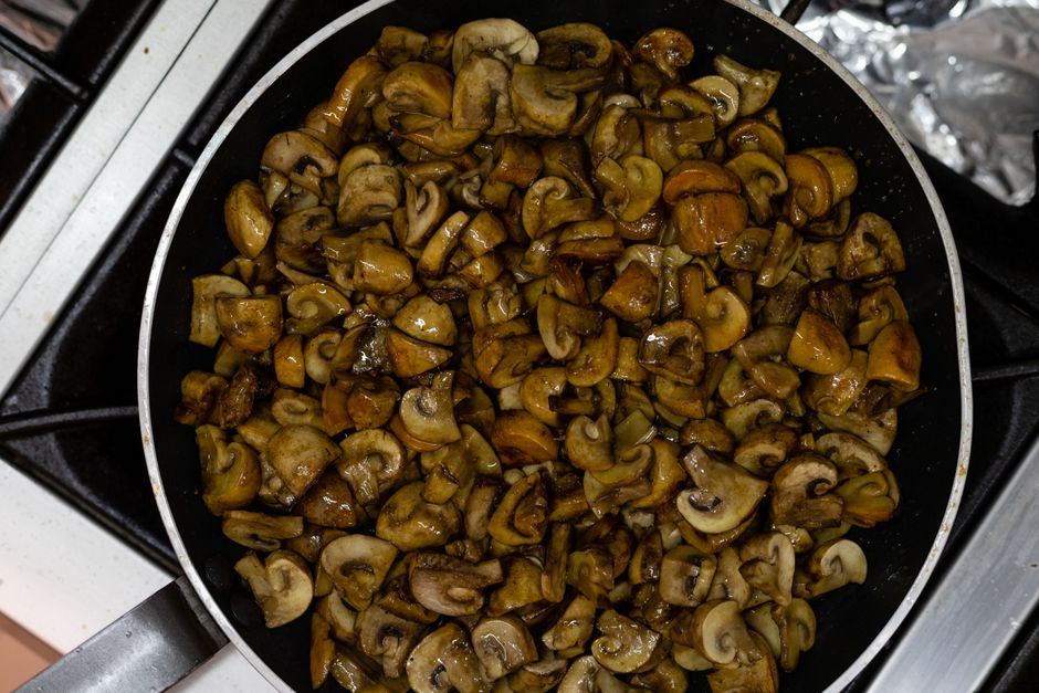 Sliced mushrooms being sautéed in a frying pan.